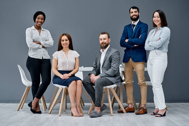 Watch us bring success to our team yet again. Portrait of a group of businesspeople posing together against a grey background - Fotografie, Obrázek