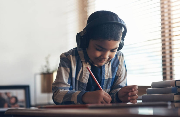 Je mehr wir spielen, desto mehr lernen wir. ein entzückender kleiner Junge, der ein digitales Tablet und Kopfhörer benutzt, während er zu Hause eine Schulaufgabe erledigt - Foto, Bild