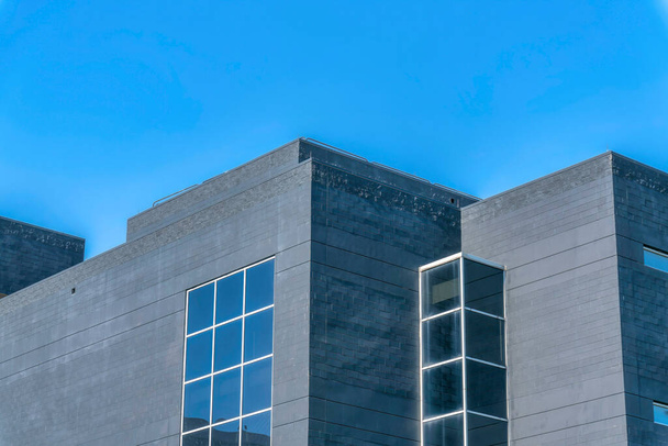 Остин, Техас - Современный внешний вид здания с серой бетонной облицовкой стен и решетчатыми окнами. Низкоугольный вид плоского здания на фоне голубого неба. - Фото, изображение