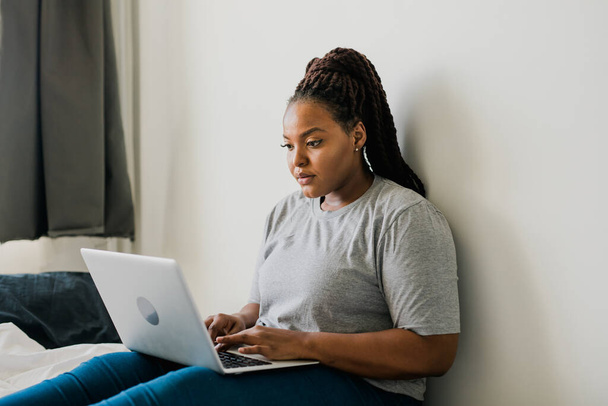 Αφροαμερικανή νεαρή γυναίκα που χρησιμοποιεί φορητό υπολογιστή στο κρεβάτι - τεχνολογίες και επικοινωνία και κοινωνικό δίκτυο - Φωτογραφία, εικόνα