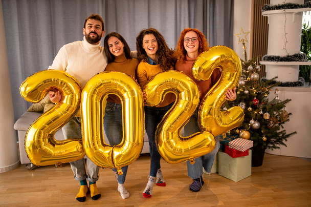 Gruppe junger schöner Menschen in lässiger Kleidung, die goldfarbene Zahlen tragen und lächeln - Foto, Bild