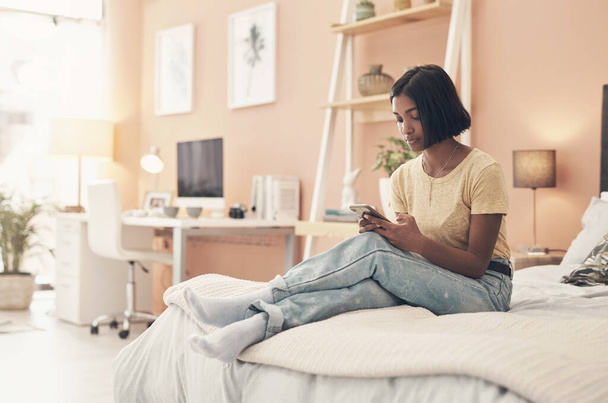 Un teléfono ocupado significa que nunca estás solo. una mujer joven usando un teléfono inteligente mientras se relaja en su cama en casa - Foto, imagen