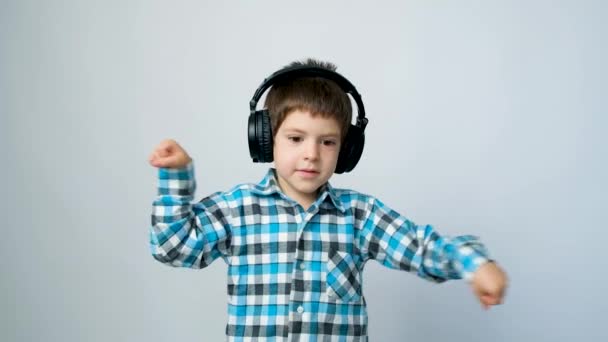 Niño de 5 años con auriculares bailando y mirando a la cámara sobre un fondo blanco. - Metraje, vídeo
