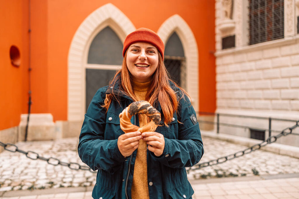 Падение туристической женщины в яркой шляпе и осенней куртке с выпечкой obwarzanek традиционной польской кухни бублик с закусками на старой городской Рыночной площади в Кракове  - Фото, изображение