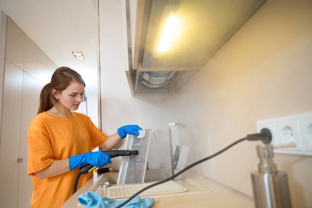 Young female in protective gloves holding metal grate from range hood and cleaning it in the kitchen - Foto, Imagem