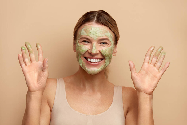 Positive Woman with Face Mask. Portrait Of Laughing Female Model Applying Natural Clay Mask On Facial Skin. Closeup Of Beautiful Happy Woman With Face Covered With Beauty Product. High Resolution  - Foto, Bild