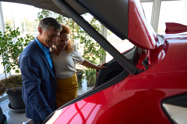 Egy pár ellenőrzi az új luxusautót az Autosalonnál. Automatikus értékesítési koncepció - Fotó, kép
