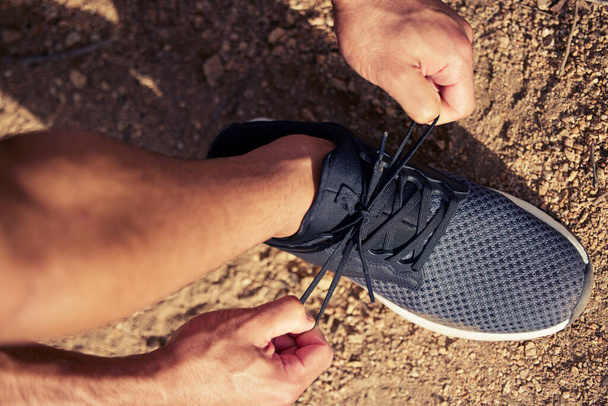 Investoida hyviä jalkineita parantaa liikuntaa. Korkea kulma laukaus tunnistamaton mies sitoo hänen kengännauhat harjoitellessaan ulkona - Valokuva, kuva