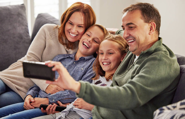 Przechwytywanie najlepszych chwil razem. szczęśliwa rodzina siedząca razem na kanapie w domu i używająca telefonu komórkowego do robienia selfie - Zdjęcie, obraz