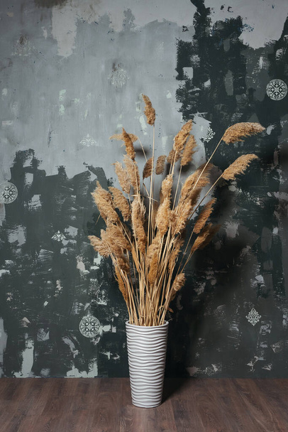 flowerpot with yellow dry flowers on a textured wall. photo zone with dried flowers in the style of minimalism. texture of putty wall with dry reed flowers - Photo, Image