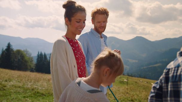 Happy parents with two children resting on summer mountains. Cheerful family spending vacation on beautiful green hill. Redhair man looking at pretty woman with kids enjoying sunny day close up.  - Foto, Imagem