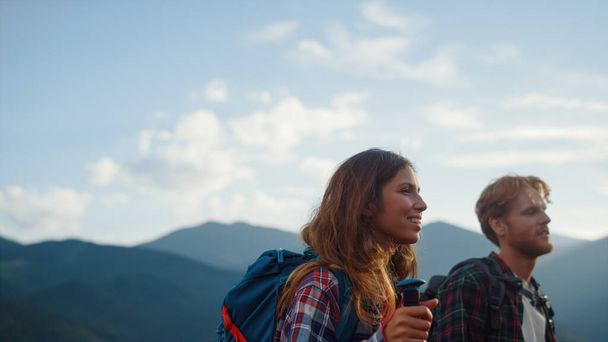 Closeup smiling couple backpack in summer mountains. Happy hikers walk nature outside. Two travelers going trekking poles on tourism destination. Young hipsters talk on sunny day. Recreation concept. - Foto, afbeelding