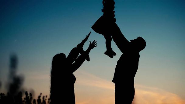 Das Konzept einer glücklichen Großfamilie. Glückliche Eltern werfen ihre Kinder vor Sonnenuntergang in die Höhe. Hochwertiges 4k Filmmaterial - Foto, Bild