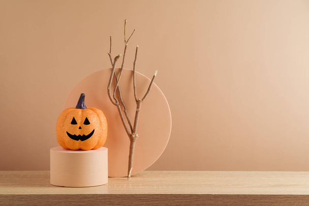 Modern still life composition for Halloween holiday. Pumpkin and tree branch on podium over beige background - Fotoğraf, Görsel