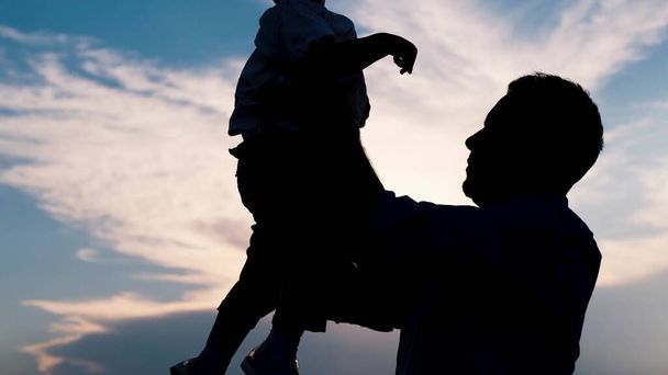 Father and son silhouette on a blue sky background. Happy family child dream concept. A father holds a child in his arms at sunset shadow silhouette. fathers day High quality 4k video - Photo, Image