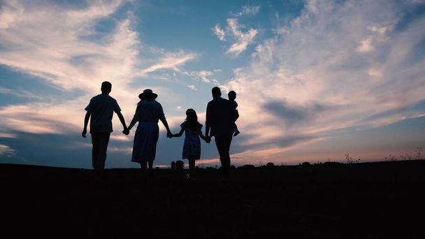 Silhouette d'une grande famille au coucher du soleil, parents avec enfants se tenant la main. Bonne famille qui s'amuse dans le parc. Silhouette familiale. Concept de famille heureuse. - Photo, image