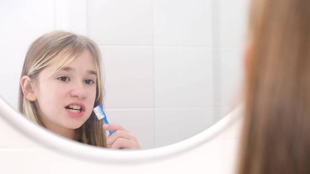 Una bambina si lava i denti con uno spazzolino da denti, un bambino si lava i denti vicino allo specchio in bagno. Concetto di denti sani - Foto, immagini