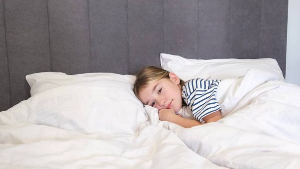 小さな女の子がベッドで横になって寝ている。8歳から9歳の少女がベビーベッドで眠りにつく。4kビデオ - 写真・画像