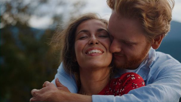Portrait of happy man hugging woman outdoor. Young affectionate couple caressing each other in summer mountains. Tender lovers enjoying family vacation on meadow. Just married honeymoon concept - Photo, Image