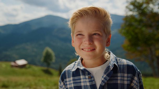 Portrait of happy boy looking camera on mountains sunny day. Carefree little man posing standing on green meadow close up. Positive cute preteen guy spending summer holiday on nature. Leisure concept. - Foto, immagini