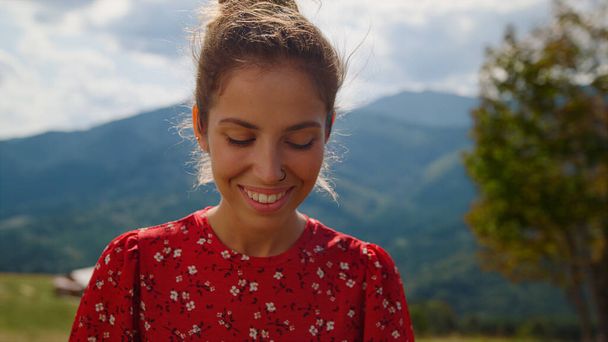 Closeup smiling pretty woman posing in front mountains summer holiday. Portrait of happy girl looking camera standing green meadow. Positive lady wearing red dress relax outdoors on sunny day. - Photo, image