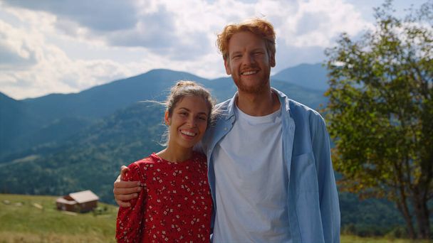 Happy couple posing in front amazing mountains looking to each other with love closeup. Cheerful man hugging pretty woman on nature sunny day. Loving pair smiling camera on summer family holiday. - Fotó, kép