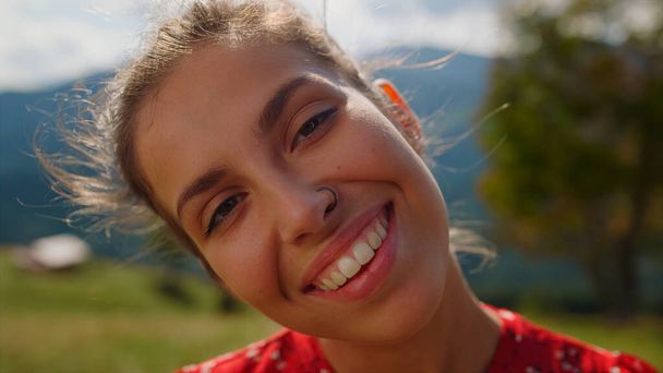 Closeup happy woman face with bright smile posing in mountains. Portrait of cheerful girl enjoying sunlight standing valley in summer holiday. Smiling lady looking camera on green meadow sunny day. - Photo, image