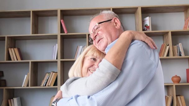 Senioren-Paar tanzt zu Hause im Wohnzimmer, sie lachen und umarmen sich, schöne romantische Senioren-Großeltern entspannen sich, haben gemeinsam Spaß zu Hause - Foto, Bild