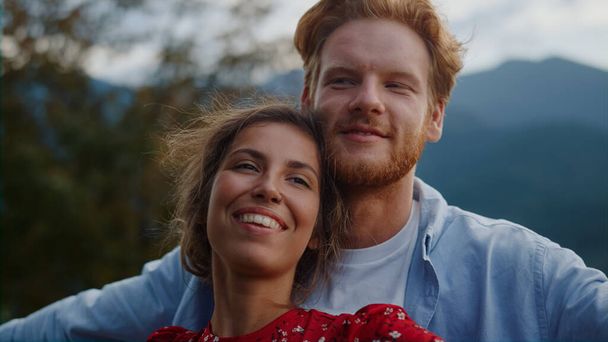幸せなカップルを一緒に屋外で抱きしめるの肖像画。山の中でデートの女性の顔に触れる生姜男。牧草地で夏休みを過ごす陽気な新しい結婚。秋の新婚旅行のコンセプト - 写真・画像