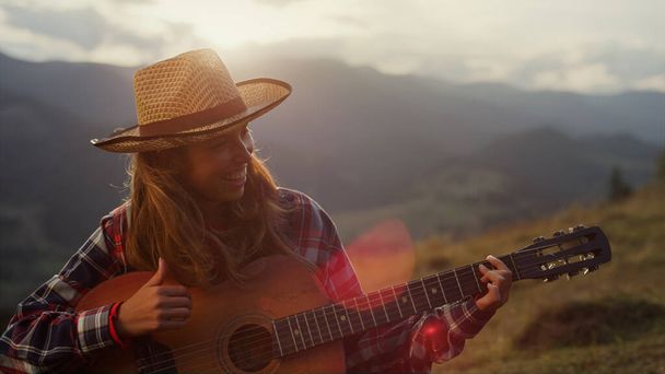 Happy guitarist smiling outdoors in mountains. Close up joyful girl play acoustic guitar. Cheerful song performer smiling enjoy summer holiday on beautiful nature. Leisure music activity concept. - Foto, immagini
