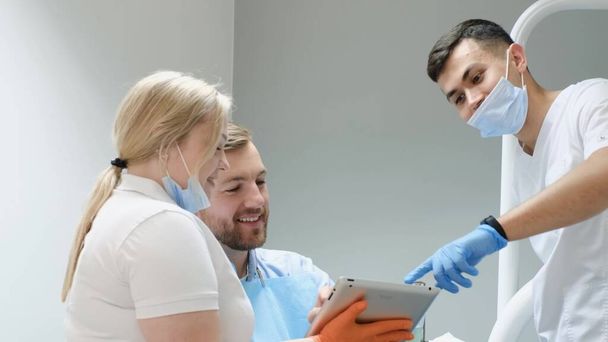 Лікар і асистент обговорюють план лікування зубів з пацієнтом. Сучасний підхід у стоматології. Хлопець, який не боїться стоматологів
 - Фото, зображення