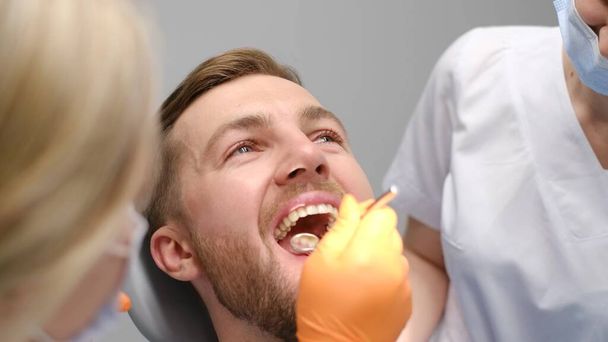Красивое лицо красивого молодого человека во время стоматологического лечения. Современный стоматологический кабинет с комфортными условиями лечения - Фото, изображение