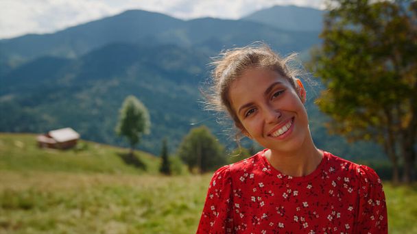 Beautiful woman feeling happy enjoy summer vacation in mountains closeup. Positive girl smiling looking camera on green meadow. Portrait of emotional model posing on nature sunny day wearing red dress - Foto, immagini