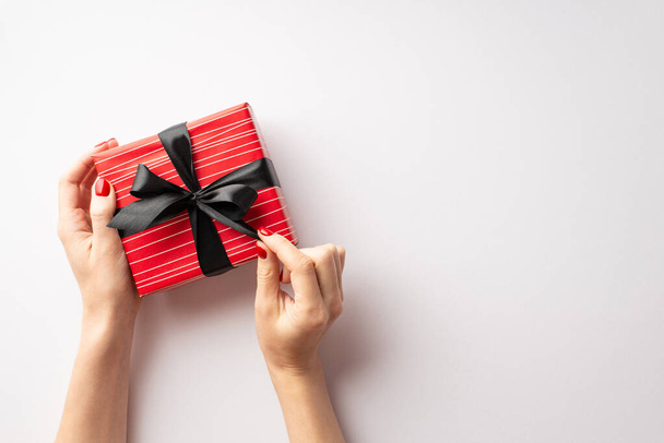 Black friday concept. First person top view photo of female hands untying ribbon bow on red giftbox on isolated white background with copyspace - Foto, Imagen