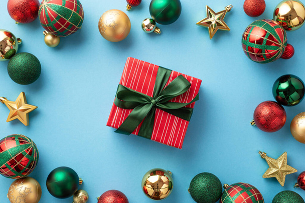 クリスマスイブのコンセプト。緑色のリボンの弓の泡と孤立したパステルブルーの背景に金の星の装飾が施された赤いギフトボックスのトップビューの写真 - 写真・画像