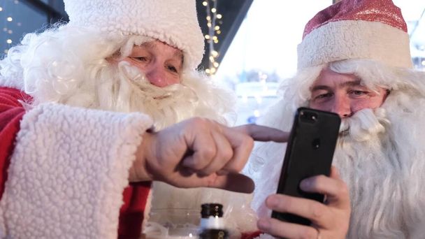 Dos personajes de Santa Claus de Navidad usan un teléfono inteligente en Nochebuena. Santa Claus se prepara para la Navidad - Foto, imagen