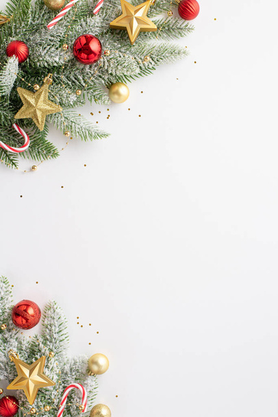 Kerstconcept. Bovenaanzicht verticale foto van dennentakken in sneeuw versierd met rode kerstballen gouden ster ornamenten snoepstokken en confetti op geïsoleerde witte achtergrond met lege ruimte - Foto, afbeelding