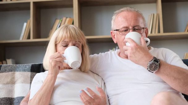 Старий чоловік і дружина п'ють каву у своїй вітальні. Час разом. Білі футболки
 - Фото, зображення