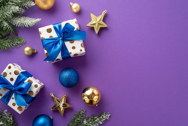 Christmas celebration concept. Top view photo of stylish gift boxes with ribbon bows blue and gold baubles star ornaments and pine branches in snow on isolated violet background with copyspace - 写真・画像