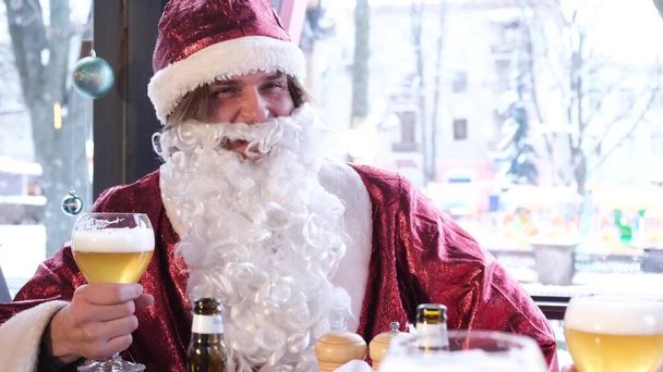Mikulás egy nagy szürke szakállú iszik sört egy pohár, ő pihen a barátaival egy kávézóban. Karácsonyi szellem, felkészülés szilveszterre - Fotó, kép