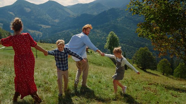 Positive parents playing outdoor games with carefree children on green sunny hill. Playful family having fun together enjoy summer holiday in mountains. Happy couple with kids fooling on nature. - Φωτογραφία, εικόνα