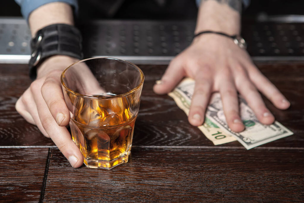 Bartender is holding out a glass of whiskey and taking the money. - Фото, изображение