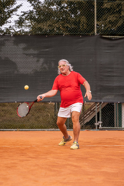Senior tennis player dressed in sportswear in action on a clay tennis court - retired wellness concept - Fotó, kép