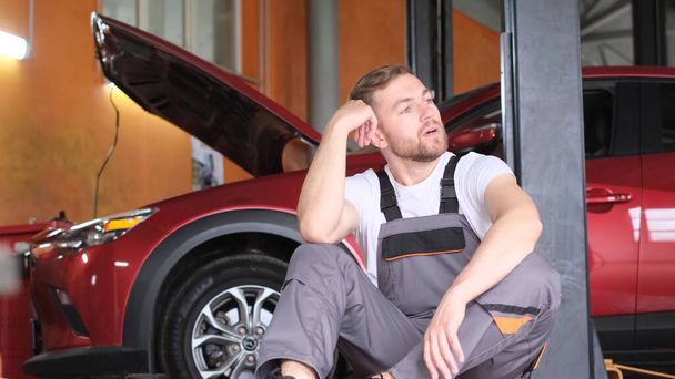 Um mecânico de carro muito cansado e frustrado está sentado em uma oficina de carros. Um homem se preocupa com falhas - Foto, Imagem