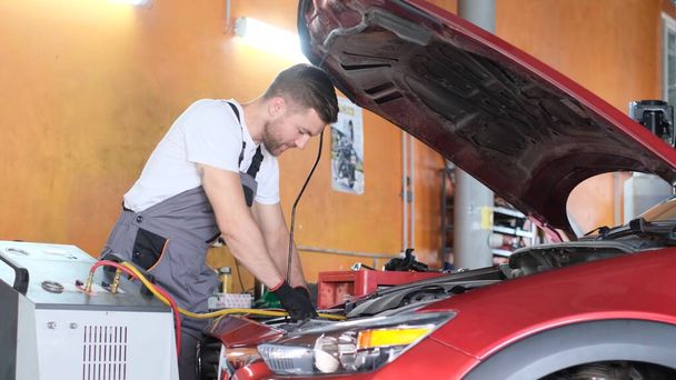 Under the hood. A man in a gray uniform is repairing a red car indoors. Timely car repair - Photo, Image