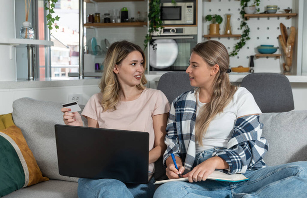 Two women, roommates and business partners, jot down and steal business ideas from the internet about what they can do with their bank credit card and start their own online company. - Valokuva, kuva