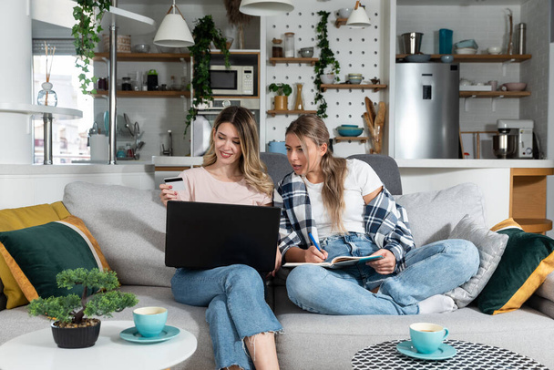 Two women, roommates and business partners, jot down and steal business ideas from the internet about what they can do with their bank credit card and start their own online company. - Foto, immagini