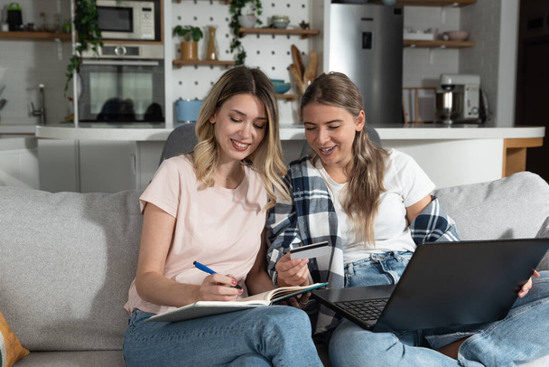 Two women, roommates and business partners, jot down and steal business ideas from the internet about what they can do with their bank credit card and start their own online company. - Photo, image