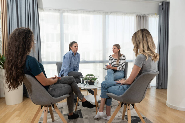 Group of women victims of robbery, violence, infidelity and other bad and negative experiences and crimes on support group psychotherapy with therapist talking about their problems. - Фото, изображение