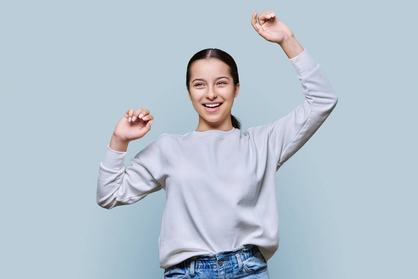 Cheerful dancing teenage girl on grey studio background. Happy young female enjoying dance music. Joy, expression, leisure, happiness, success, victory, fun, good mood concept - Photo, Image